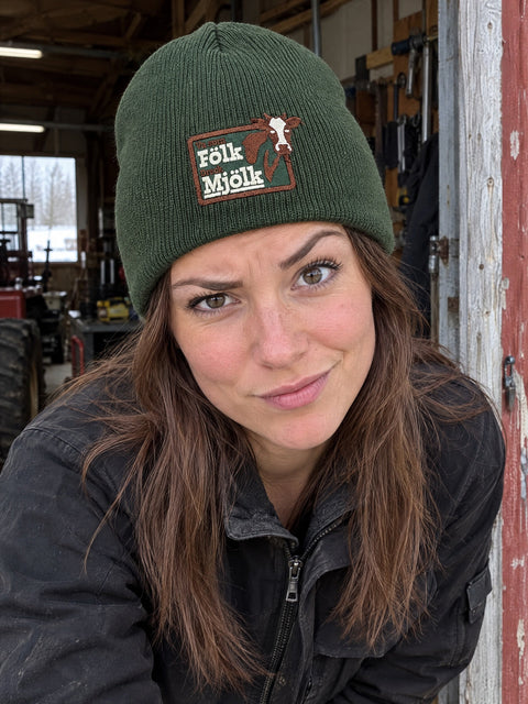 Va som Fölk Dreck Mjölk på olivgrön Hatitude Beanie, buren av en yngre vuxen.